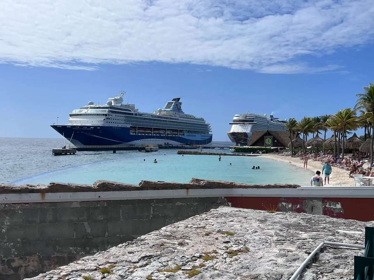 Two cruise ships docked at Curacao port with beach and resort area in foreground